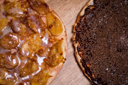 Sweet pizzas. One of banana and one of chocolate on wooden background. View from the top.の写真素材
