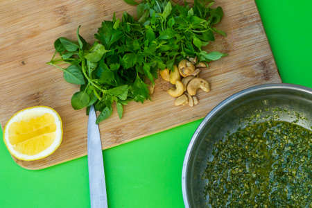 Pesto sauce. Composition on green background with bowl of fresh pesto sauce the ingredients, tomato, onion, basil are on the wooden board.の写真素材
