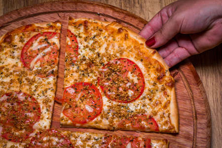 hand holding slice of pizza with roasted garlic and tomato.の写真素材