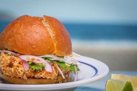 delicious fish burger with salad, onion and lemon with the beach in the background
