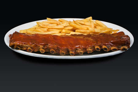 Prime rib with barbecue sauce and french fries in a white dishware on black backgroundの写真素材
