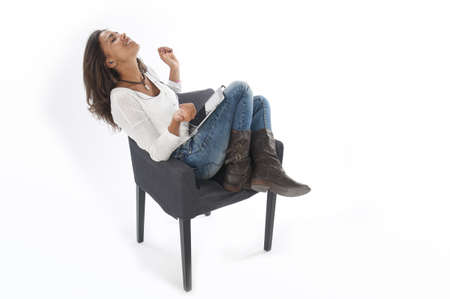 Happy young girl wearing casual clothing, on white, sitting on sofa holding tablet PC, listening to music.の写真素材