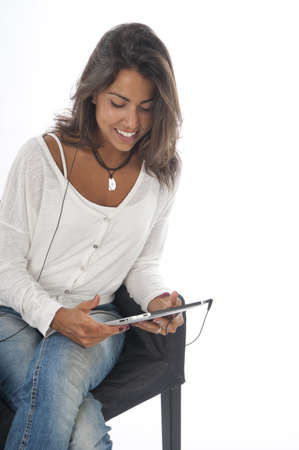 Happy young girl wearing casual clothing, on white, sitting on sofa holding tablet PC with headphones.の写真素材