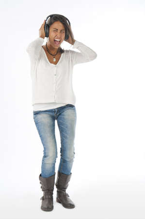 Happy young female adult with headphones, enjoying singing with open mouth and dancing, while listening to music.の写真素材