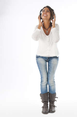 Full length portrait of young girl with casual clothing, on white, shouting with open mouth and hands on head phones, enjoying music の写真素材