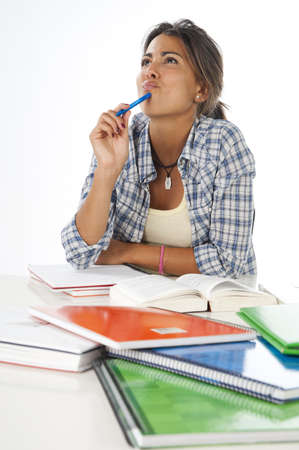 Young girl studying while daydreaming on table with books and notebooks.