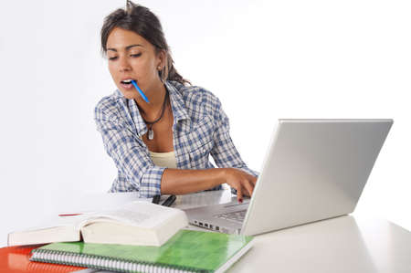 Young female student concentrated studying with laptop, books and notebooks on table.の写真素材