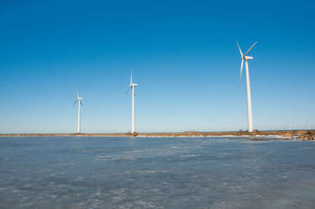 Three windmills in a row standing near seaside and frozen lake on sunny day, copenhagen, oresund,...