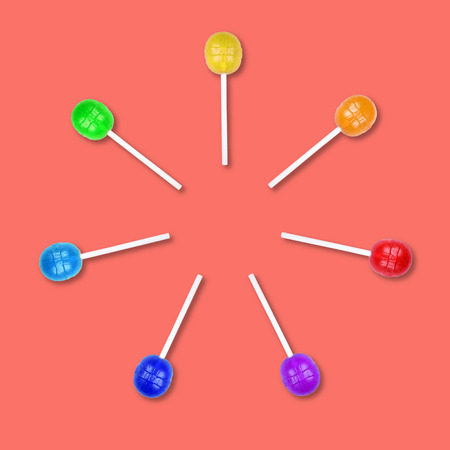 Set of colorful lollipops grouped in a circle isolated on coral background. Candy on a stick. Food background. Flat lay.の写真素材