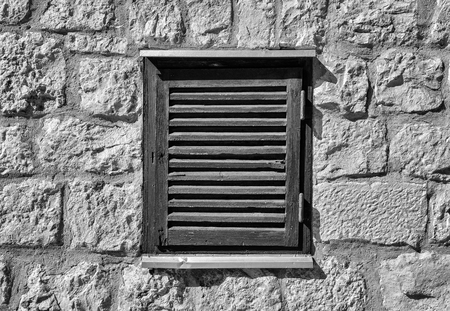 Beautiful old window frame with old wooden shutters on ancient pale rock wall. Rural antique window frame. Design element. Template or mock up.の写真素材