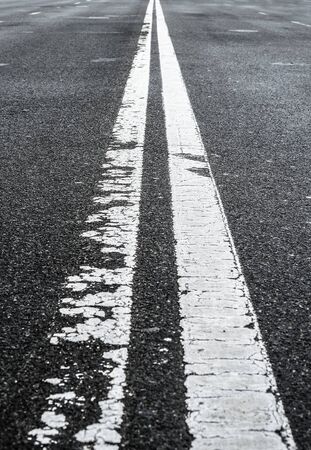 Asphalted road with two continuous faded white strips. White road divider lines of a highway. Long banner format. Two-way asphalt road, close up of the dividing road strip.の写真素材