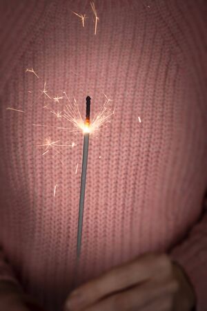Close up of girl hands holding sparkler. Happy New Year concept. Girl a pink knitted sweater hold sparkler, dark backgroundの写真素材