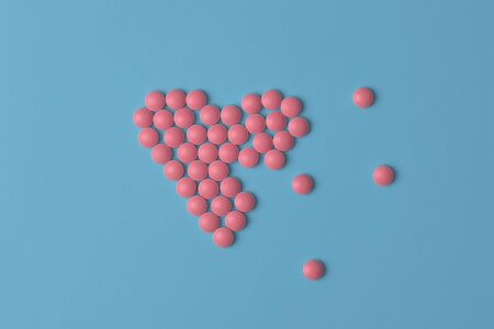 Medical background or banner. Pink Pills in form of broke heart on blue background. Flat lay. Heart health concept.の写真素材