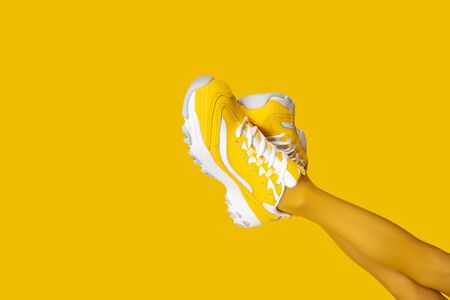 New Yellow female sneakers on long woman legs isolated on yellow background. Monochrome pop art concept. Copy space.の写真素材