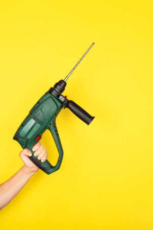 Green Puncher in the hands of a builder. Female hand hold new Puncher or drill isolated on yellow backgroundの写真素材