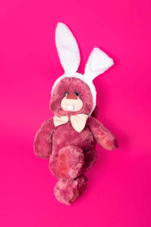 Funny and fluffy toy pink bunny in white fluffy bunny ears hoop isolated on pink background. Happy easter conceptの写真素材