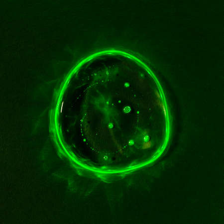 Clear transparent liquid gel dark green drop or smear with neon light green flare isolated on dark...