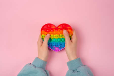 Hands playing with Pop It Antistress game fidget. Pop Fidget Sensory Toy for Autism Special Needs Stress Relief in form of heart. Silicone Pressure Relieving Toy for Kids, Children, Adults.の写真素材