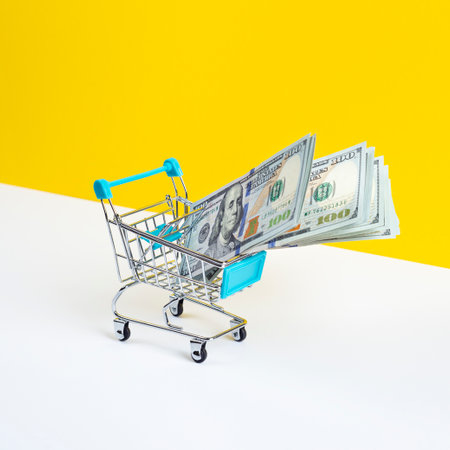 Toy supermarket cart or shopping trolley full of money isolated on yellow background. Money loan or sale concept.の写真素材