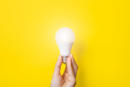 Hand holding a LED light bulb on bright yellow background. Using economical and environmentally friendly light bulb concept. Idea concept. Energy saving lamp in womans hand. Banner with copy space.の写真素材
