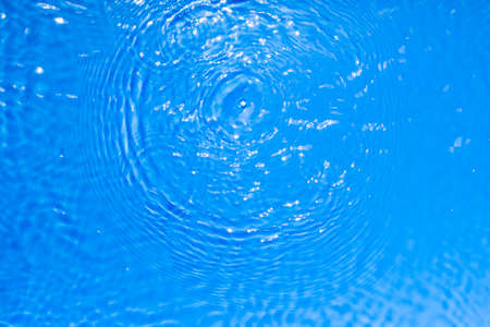 Surface of blue transparent swimming pool water texture with circles on the water. Trendy abstract nature background. Water waves in sun light reflectionsの写真素材