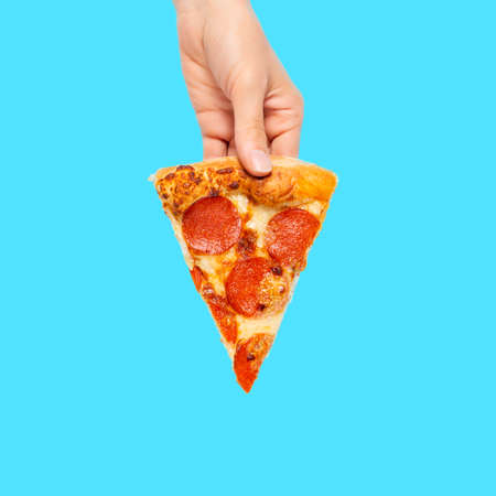 Slice of pepperoni pizza in hand isolated on blue. Top view on paperoni pizza. Concept for italian...
