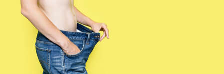 Concept of diet, proper nutrition, weight loss Slim Woman Showing Loose Jeans and her Loss Weight. Woman in oversize jeans isolated on yellow background Banner with copy space. Banner with copy space.の写真素材