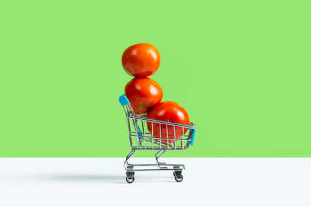 Toy shopping cart or trolley full of large red tomatoes isolated on green background. Fall harvest sale concept. Banner with copy space.の写真素材