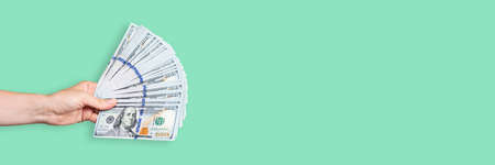 Hand holding a big stack of banknotes isolated on light green background. Wealth or loan concept....