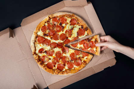 Hand taking a slice of pizza from pizza box. Big Hawaii pizza without one piece. Top view on Hawaii pizza. Concept for italian food, street food, fast food, quick bite.の写真素材