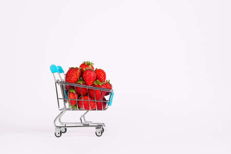 Toy shopping cart or trolley full of ripe large red strawberries isolated on white background. Berry harvest sale concept. Banner with copy space.の写真素材