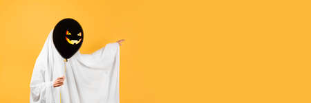 Halloween concept. Girl in a funny ghost costume with a black balloon with Jack lantern or scary...