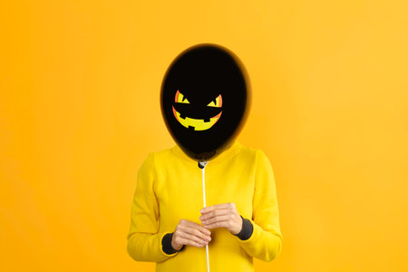 Halloween concept. Girl holding black balloon with Jack lantern or scary pumpkin face isolated on...