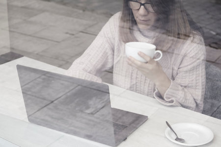Young attractive woman working on laptop in modern coworking space and drinking cocoa. Elerning or...