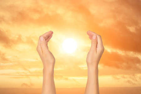 Open palms holding sun on background of sunset sky. Travel and inspiration, meditation concept.の写真素材