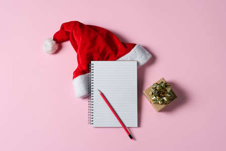 New year wish list concept. Notepad, Santa Claus hat and gift box isolated on pink background....
