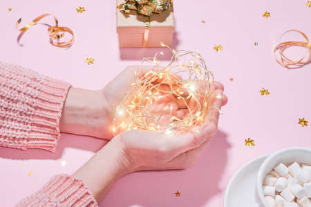 Beautiful and cozy holiday concept Hands holding string garland lights, on the background of wrapped...