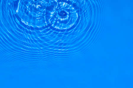 Surface of deep blue transparent swimming pool water texture with circles on the water. Trendy...