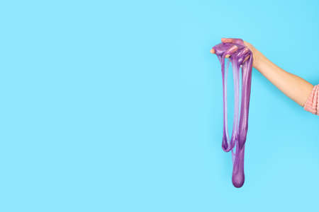 Close up on shiny purple or violet slime in the hand isolated on blue background. Fun and stress relief concept. Banner with copy space.の写真素材