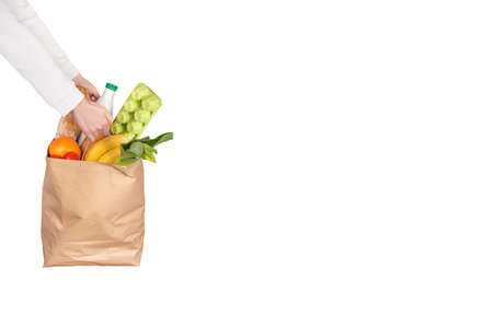 Food delivery, online shopping or donation concept. Grocery store shopping. Courier holds a paper bag filled with groceries isolated on white background. Banner with copy space.の写真素材