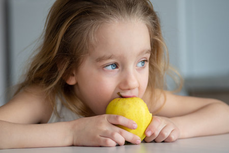 Portrait of a little blond girl smiling and eating an apple. The concept of healthy eating for children.の写真素材