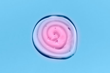 Light blue and pink round gradient transparent gel drop isolated on blue background. Top view. Virus protection or cosmetics concept. Face Serum texture close up.の写真素材