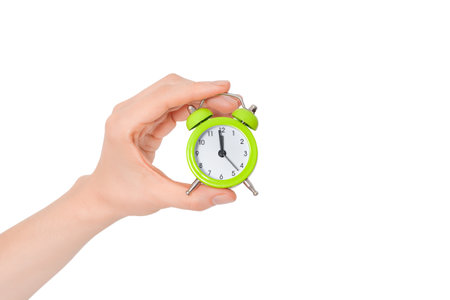 Hand holding a small alarm clock. The concept of time management. Green Alarm clock on a white...