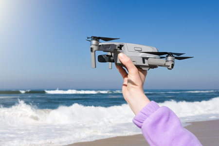 Hand holding drone ready to take off on the background of stormy Atlantic Ocean. Drone in hand.の写真素材