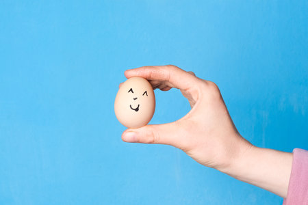 Hand holding easter egg with a funny face drawn on it. Easter or healthy diet eating concept.の写真素材