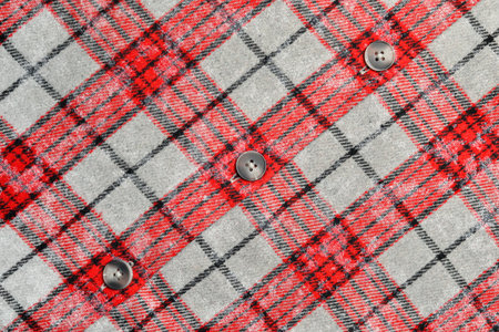 Close up of red and black tartan plaid fabric with gray background, featuring four black buttons. Perfect for fashion, textile, or pattern design projects.の写真素材
