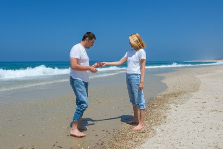 A couple stands on a sandy beach, with the man proposing to the woman, as waves crash in the background.の写真素材