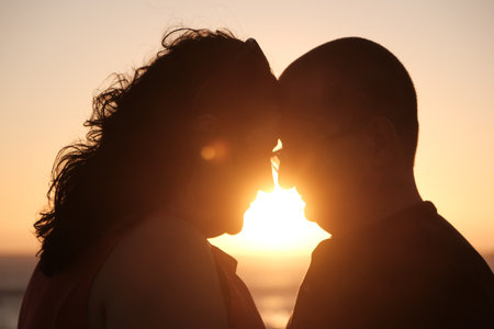 Mature couple touching foreheads in a tender moment at sunset with warm golden light creating a romantic silhouette.の写真素材