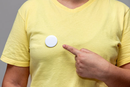 Woman in yellow shirt pointing at a shiny round button. Isolated pin badge mockupの写真素材