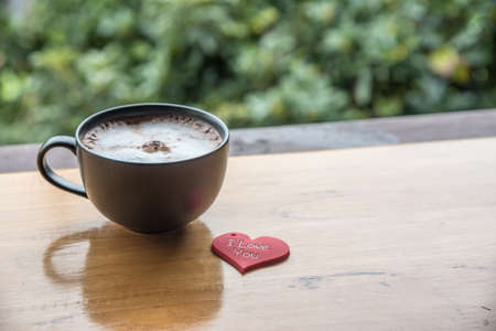 Red heart shaped note I love you with cup of hot coffee on wooden background and morning sunlight....